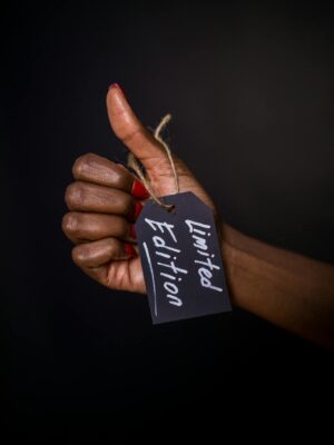 Close-up of a hand with a limited edition tag, thumbs up gesture against dark background.